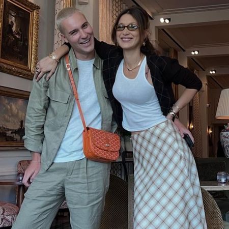 Bella Hadid poses with a friend wearing a knee-length skirt with knee-high boots with a tank-top and cardigan.