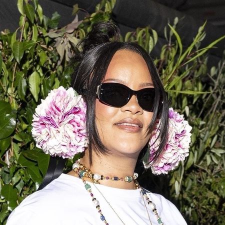 Rihanna wearing pink earmuffs, a white t-shirt, blue jeans, a white scarf, and pink satin heels