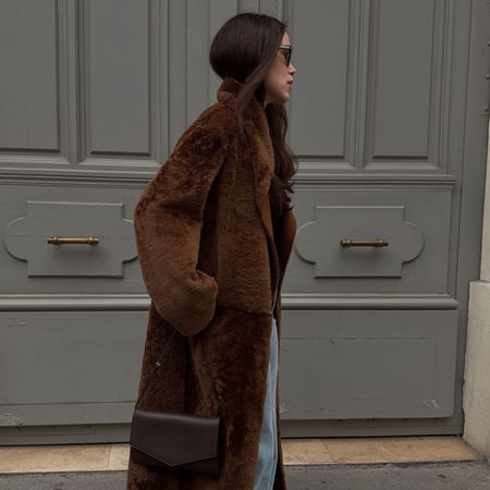 Woman wears brown faux fur coat, blue jeans and burgundy bag