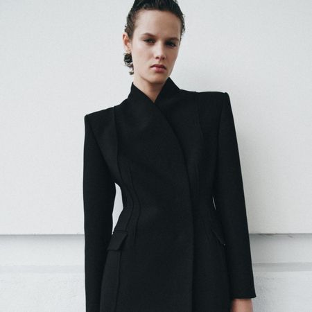 Model wears black blazer with high neck and fitted waist