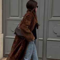Woman wearing brown fur coat, straight leg denim, and brown bag while walking on the streets of Paris, France